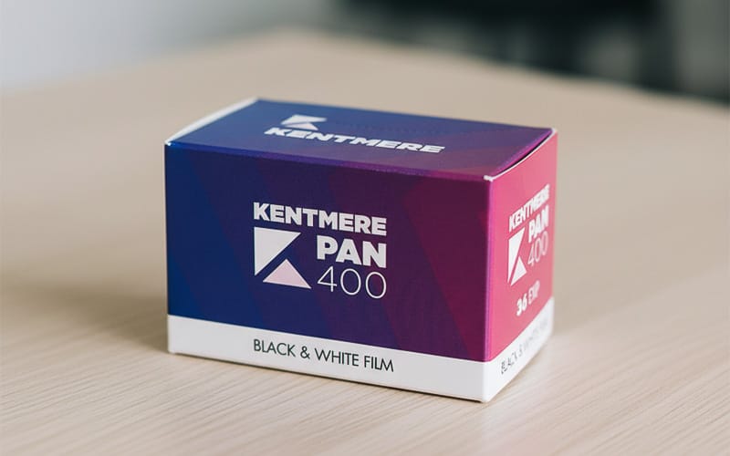Kentmere Pan 400 black and white film box with a blue and pink gradient design, resting on a wooden surface.